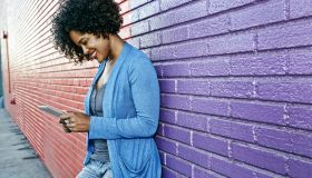 Mixed race woman with cell phone standing by colorful wall