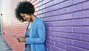 Mixed race woman with cell phone standing by colorful wall