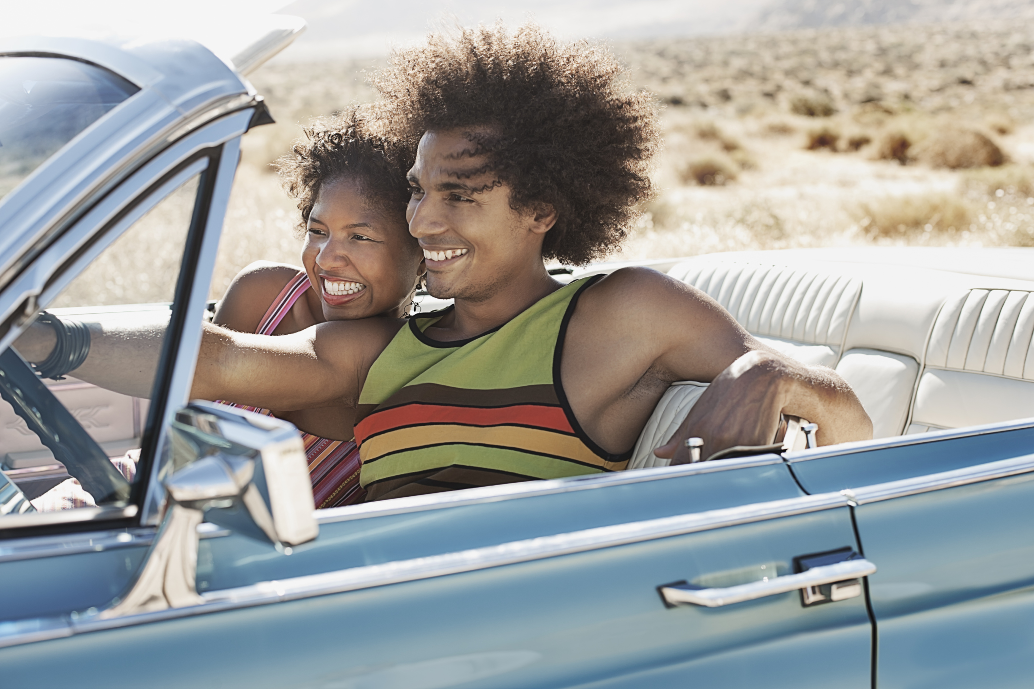A young couple, man and woman in a pale blue convertible on the open road