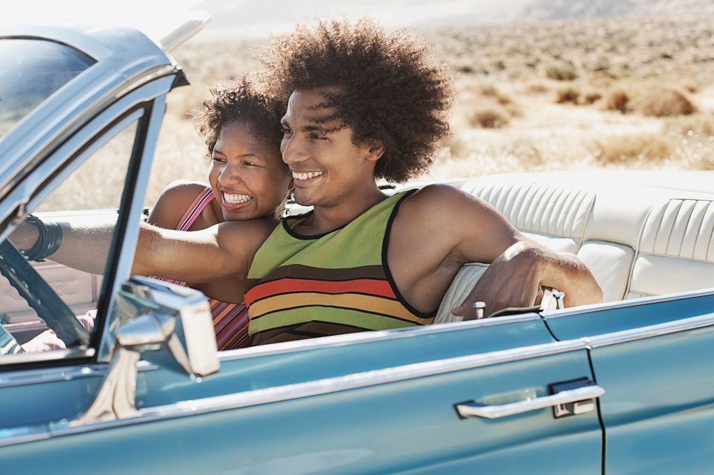 A young couple, man and woman in a pale blue convertible on the open road