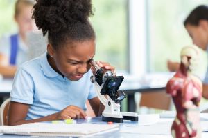 Beautiful elementary schoolgirl uses a microscope for science project