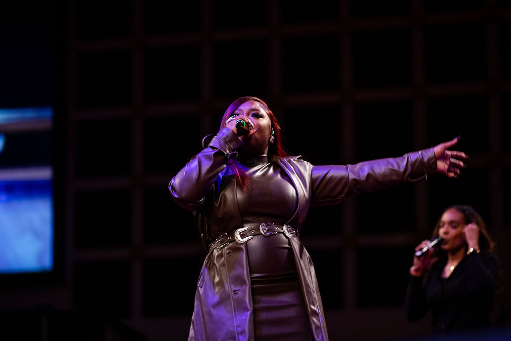 A woman in a purple outfit performing on stage with her arms outstretched.
