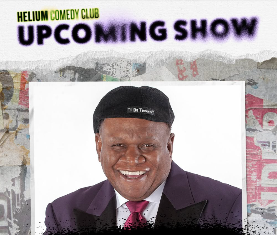 A smiling African American man wearing a black cap that says "I Be Thinkin'" and a purple suit jacket, against a background of a Helium Comedy Club upcoming show poster.